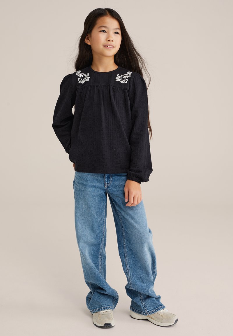 Pikad mustad tekstuuriga topp valgete lillepärlitega õlgadel, kombineeritud helesiniste laiade pükstega ja hallide tossudega.