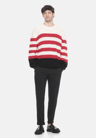 Maglione a righe in crema, rosso e nero, con collo a giro e spalle ribassate. Abbinato a pantaloni neri e scarpe nere.