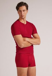 Camiseta roja ajustada y bóxers a juego en un tejido suave y elástico. La camiseta presenta un cuello redondo y mangas cortas.