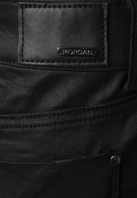 Jeans in denim nero con una superficie testurizzata e un'etichetta in pelle cucita con il marchio "MORGAN" sul retro. Finiture in argento visibili.
