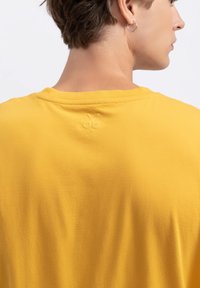 Geel katoenen t-shirt met een eenvoudig ontwerp, met een klein geborduurd schaar detail bij de halslijn. Glad textuur en ontspannen pasvorm.