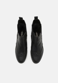 Botas de tobillo de cuero negro con detalles de brogue, con un corte suave y acentos texturizados. Tiradores en el tobillo para facilitar su uso.