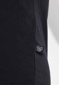 Zwarte katoenen T-shirt met een soepele textuur. Zijaanzicht toont een stoffen label dat in de zoom is gestikt. Eenvoudig ontwerp, zonder zichtbare patronen.