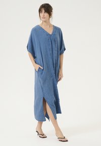 Zils šambrey kleita ar V veida kaklu, īsām piedurknēm, sānu kabatām un augstu šķēlumu, izgatavota no teksturēta viegla auduma.