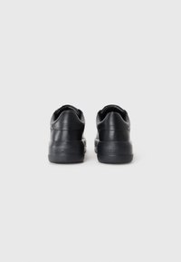 Black leather sneakers with a rounded back, textured heel, and thick sole; features embossed branding on the heel.