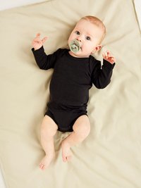 Svart långärmad body på en baby som ligger på en beige bakgrund. Babyn har en grön napp och ljusbrunt hår. Armarna är lyfta och fötterna är synliga.