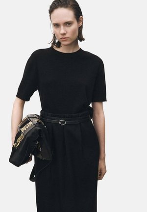 Haut noir en tricot à manches courtes associé à une jupe plissée noire et un sac noir, avec un design structuré et des accents métalliques.