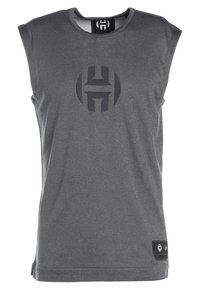 T-shirt de sport sans manches gris avec une texture lisse. Présente un logo foncé bien visible à l'avant et une petite étiquette en bas à gauche.