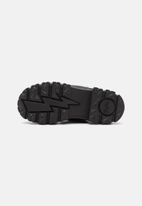 Black rubber sole with deep treads, featuring a zigzag pattern and raised accents. Durable design suitable for various terrains.