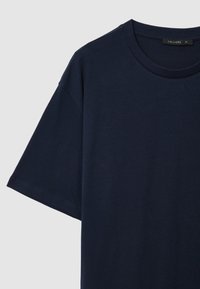 T-shirt in cotone blu navale a maniche corte con colletto rotondo e etichetta "Calliope XL" su sfondo grigio chiaro.