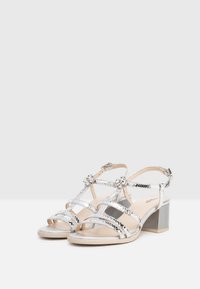 Sandali argentati con cinturini, dotati di tacco a blocco, caratterizzati da una texture lucida a pelle di serpente, dettagli floreali e una soletta di colore beige chiaro.