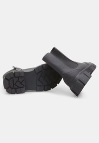 Botines negros hasta el tobillo con un acabado mate, paneles laterales elásticos y suelas rugosas y antideslizantes. Diseñados para la durabilidad y la comodidad.