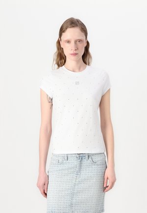 T-shirt blanc à manches courtes avec un col rond, présentant de petits accents brillants et un logo subtil sur la poitrine. Associé à une jupe en denim à motifs.