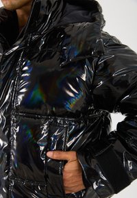Black puffer jacket with a glossy, reflective finish, featuring a hood, large front pockets, and textured cuffs with Velcro closure.
