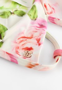 Lilleline ujumispealne pastellvärvides, sileda kangaga, millel on roosa ja rohelise roosi mustrid. Ühel küljel on väike metallist logoetikett.