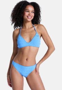 Σετ μπικίνι σε ανοιχτό γαλάζιο χρώμα με τοπ σε σχήμα τριγώνου και ταιριαστή βερμούδα. Και τα δύο κομμάτια έχουν υφή με κυματιστό μοτίβο. Το υλικό φαίνεται μαλακό και ελαστικό.