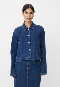 Veste en denim bleu foncé avec un col chemise, une fermeture à boutons sur le devant et des accents de double couture. Comprend des poches latérales et des manches longues.