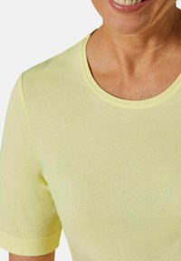 Helles, gelbes Kurzarmhemd mit rundem Halsausschnitt, aus weichem Stoff gefertigt. Die Nahtdetails sind dezent und sorgen für einen glatten, lässigen Look.