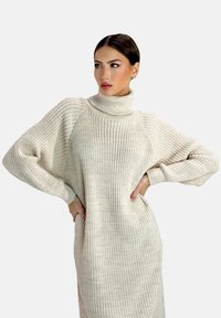 Vestito maglione a coste color crema con collo alto, maniche oversize e vestibilità rilassata. Presenta tasche laterali e un motivo testurizzato.