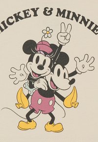 Gráfico de Mickey y Minnie Mouse en tela crema. Diseño de dibujo animado colorido que presenta poses juguetonas y acentos brillantes en rosa, negro y amarillo.