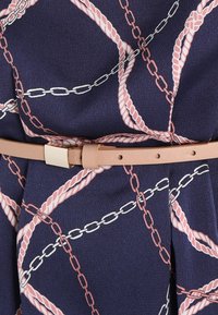 Tela azul marino con un patrón de cadenas y cuerdas en rosa y blanco, que presenta un cinturón marrón claro con una hebilla rectangular en tono dorado.
