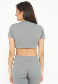 Grå ribbet crop top med korte ærmer, tætsiddende design og en matchende højtaljet leggings med elastisk linning og logo-detalje.