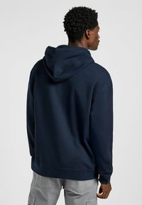 Sudadera con capucha de color azul marino con un acabado texturizado, que cuenta con una capucha ajustable y puños acanalados, combinada con pantalones cargo de color gris claro.