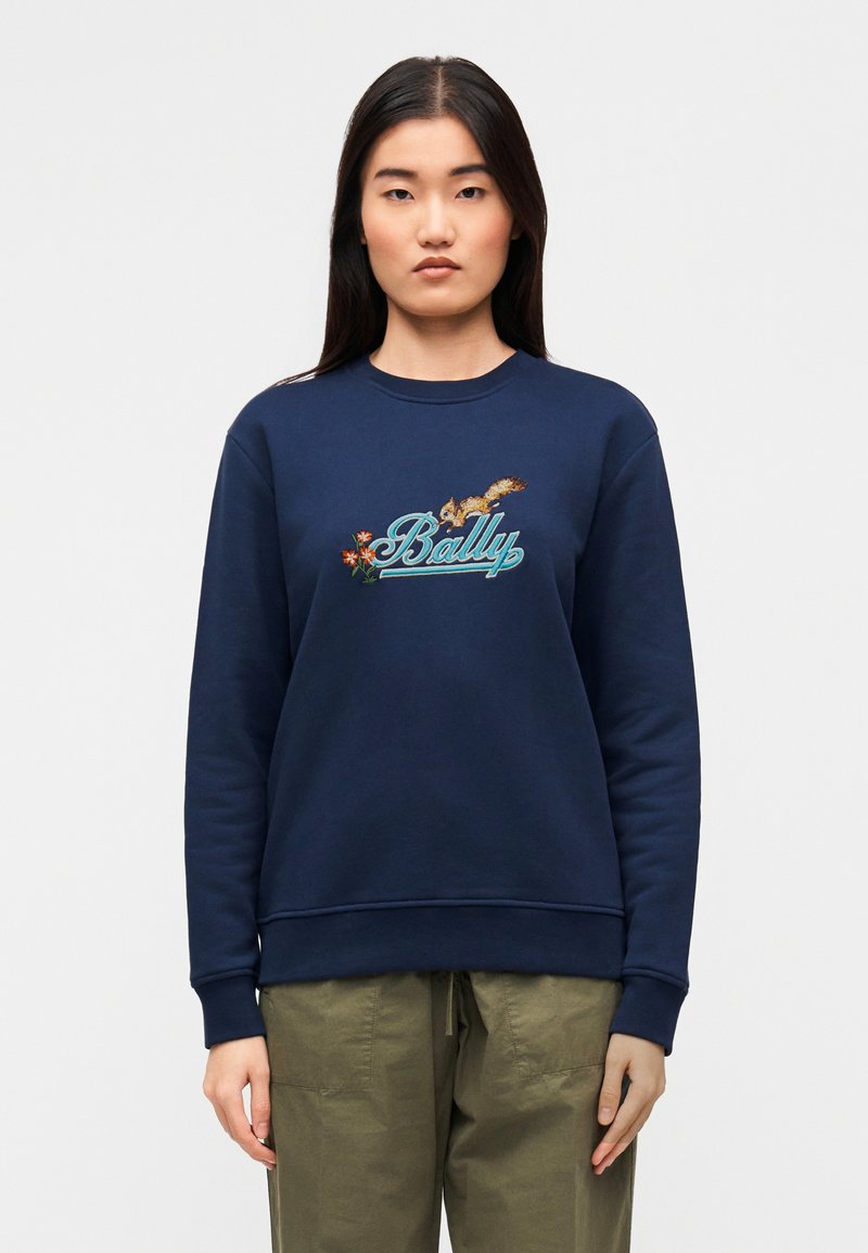 Μπλε σκούρο φούτερ με κεντημένο λογότυπο "Bally", λουλουδάτες λεπτομέρειες, ριμπ μανσέτες και στρογγυλή λαιμόκοψη. Συνδυάζεται με παντελόνι ελιάς.