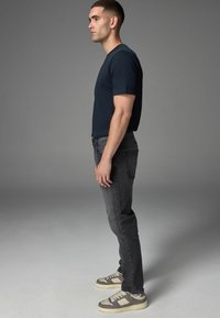 Dunkles Kurzarm-T-Shirt kombiniert mit grauen Jeans und beigen Sneakers. Die Silhouette ist schlank, mit einem einfachen, klaren Design und glatter Textur.