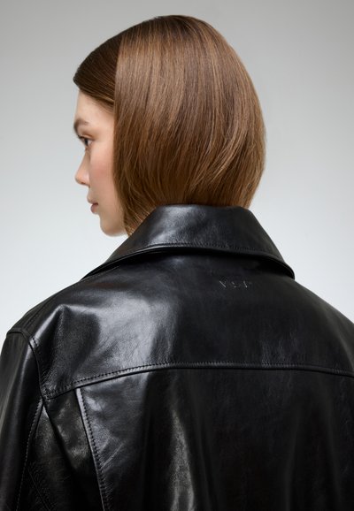 Black leather jacket with a smooth texture, wide collar, and subtle embossed logo on the back. View from the side, highlighting the neckline.