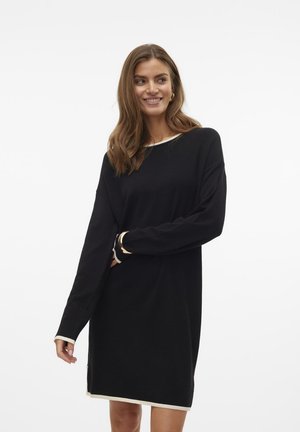 Robe pull noire avec des manches longues, un large col et des accents crème sur les poignets et l'ourlet. Tissu doux, coupe décontractée.