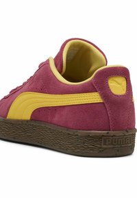 Puma sporta apavi ar bordo zamšādas virsu, dzeltenā akcentos un teksturētu brūnu gumijas zoli. Iezīmēts ar logotipu uz papēža un mīkstu apkaklīti.