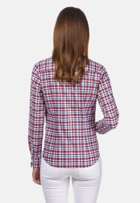 Long-sleeve button-up shirt in a multicolor plaid pattern with red, blue, and white squares, finished with a curved hem and fitted shape.