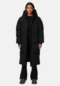 Czarna długa kurtka puchowa z kapturem, z zamkiem błyskawicznym i dużymi pikowanymi sekcjami. Nosi się ją na ciemnym stroju, a materiał wydaje się gładki.