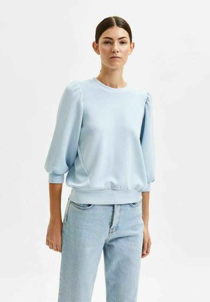 Felpa azzurra con maniche a sbuffo, scollatura rotonda e orlo a costine. Abbinata a jeans azzurri. Tessuto morbido, vestibilità casual.