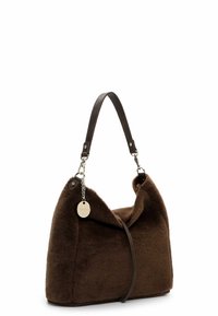 Sac bandoulière en tissu doux marron avec une sangle en cuir foncé et une étiquette ronde argentée attachée par une chaîne sur un côté.