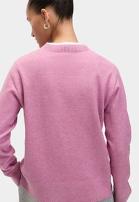 Maglione rosa con polsini e orlo a coste, realizzato in un tessuto morbido. Il retro presenta un collo a giro e dettagli minimi.