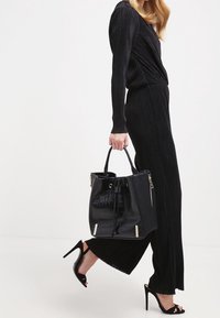 Bolso tote negro con estampado de cocodrilo y forma estructurada, con dos asas superiores y acentos metálicos. Llevado con un conjunto negro con plisados y tacones.