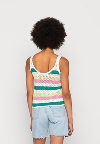 Szydełkowy top na ramiączkach w pastelowe różowe, zielone i białe paski. Posiada falbaniaste ramiączka i dół, a także luźny, lekki krój. Połączony z dżinsowymi szortami.