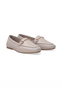 Beige leren loafers met een platte zool, voorzien van een goudkleurige hakespe-detail op de bovenkant en een gladde, matte afwerking.
