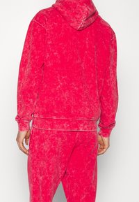 Sudadera de forro polar en un rosa vibrante con una apariencia texturizada y ligeramente desgastada. Presenta una capucha con cordón y puños y dobladillo acanalados.