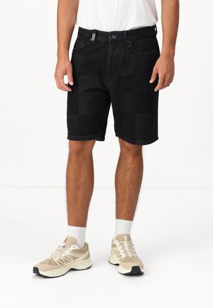 Shorts in denim nera con un motivo a scacchi, leggera usura, design a cinque tasche e vita standard. Indossati con sneakers beige.