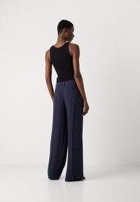 Top sans manches noir associé à un pantalon large à rayures navy, avec une texture lisse et une coupe classique avec poches arrière.