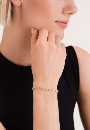 Bracelet en or au design délicat, comportant une rangée de pierres précieuses transparentes étincelantes, porté sur un poignet, avec une peau lisse visible.