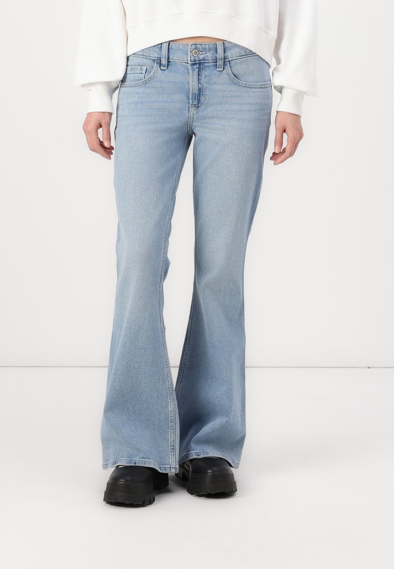 Jeans acampanados de color azul claro, fabricados en denim, con una cintura de altura media y un ligero desvanecimiento. Combinados con zapatos de suela gruesa negra.