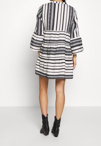 Robe à rayures noires et blanches avec volants superposés, manches volumineuses et motifs texturés. Associée à des bottines noires.