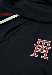 Tela de color azul marino con un acabado texturizado, que presenta un logotipo rojo y blanco prominente en la parte inferior y rayas en contraste en el escote.