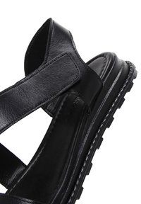 Sandalo in pelle nera con larghe cinghie, suola imbottita e battistrada testurizzato. Il design enfatizza il piede scoperto per una migliore traspirabilità.