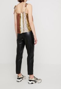 Top senza maniche con multi-patter e spalline sottili; presenta stampe animali in tonalità di marrone, crema e oro. Abbinato a pantaloni in pelle nera e sneakers.