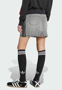 Falda de mezclilla gris con cintura alta, cinco bolsillos y rayas laterales. Combinada con calcetas negras hasta la rodilla que tienen rayas blancas y un logo.